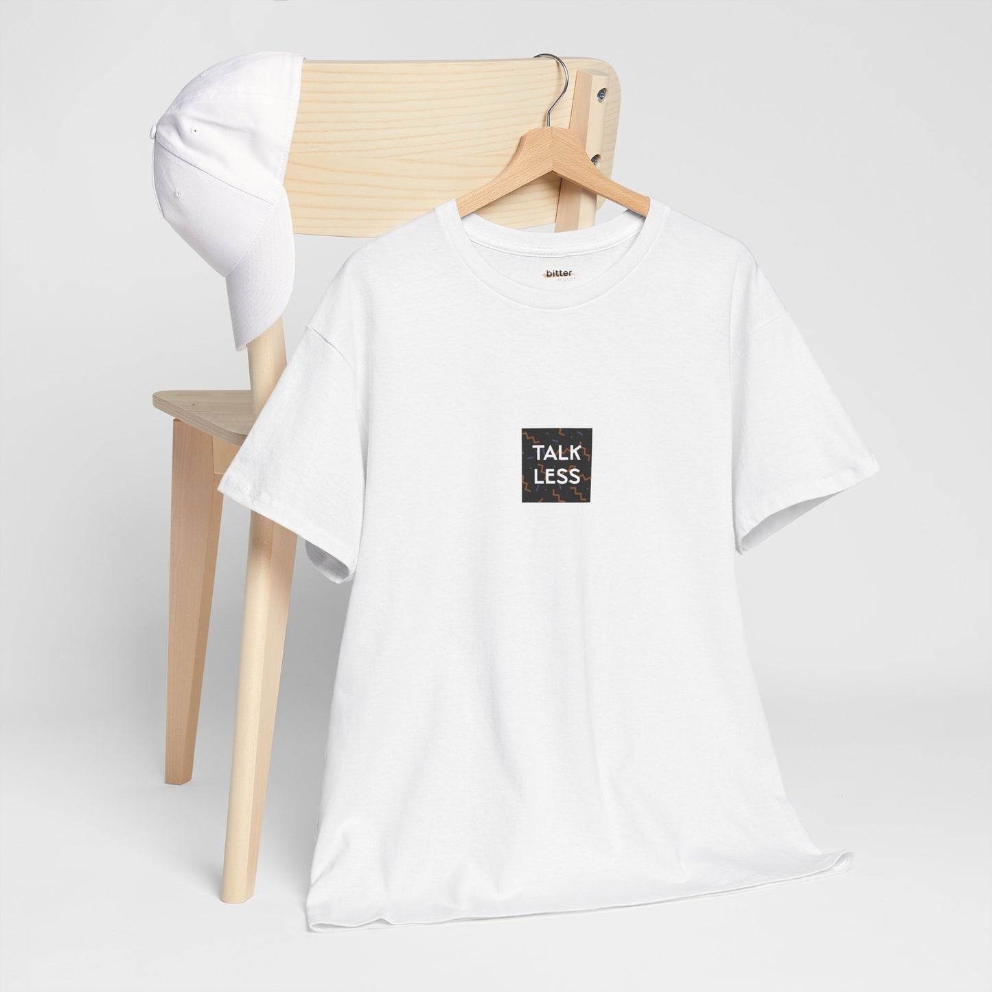 White t-shirt with 'Talk Less' print on a wooden chair against a white background
